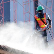 Worker in safety vest cleaning roof tiles with high pressure cleaning machine. Roof cleaning with high pressure water jet
